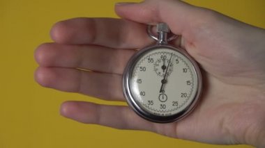 Sarı arka planda analog kronometre tutan bir kadın eli..