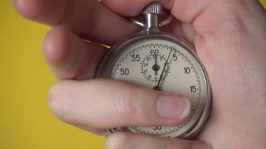 Sarı arka planda analog kronometre tutan bir kadın eli..