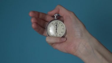 Bir kadının elinde mavi renkli bir ekranda analog bir kronometre var..