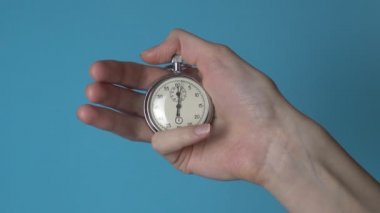 Bir kadının elinde mavi renkli bir ekranda analog bir kronometre var..