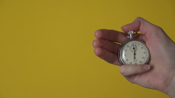 Die Hand einer Frau hält eine analoge Stoppuhr auf gelbem Hintergrund. — Stockvideo