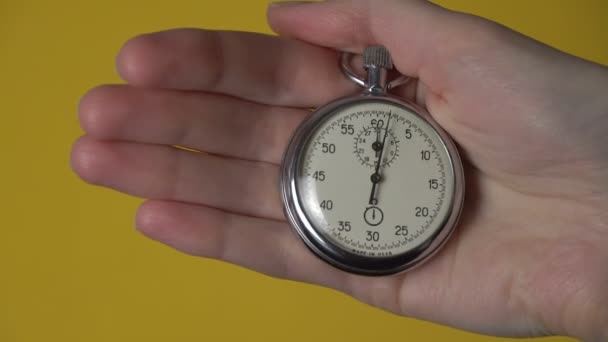 La mano de una mujer sostiene un cronómetro analógico sobre un fondo amarillo. — Vídeos de Stock