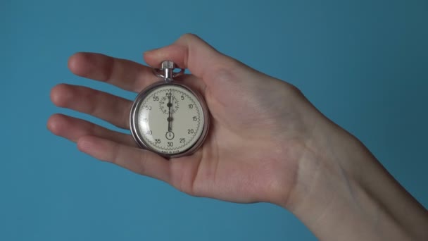 De hand van een vrouw houdt een analoge stopwatch op een blauw chromakey scherm. — Stockvideo