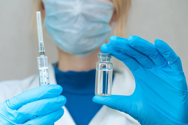 身穿白衣 戴着面具和蓝色手套的女医生一只手拿着注射器 另一只手拿着装有疫苗和药物特写的瓶子 药品和疫苗接种的概念 — 图库照片