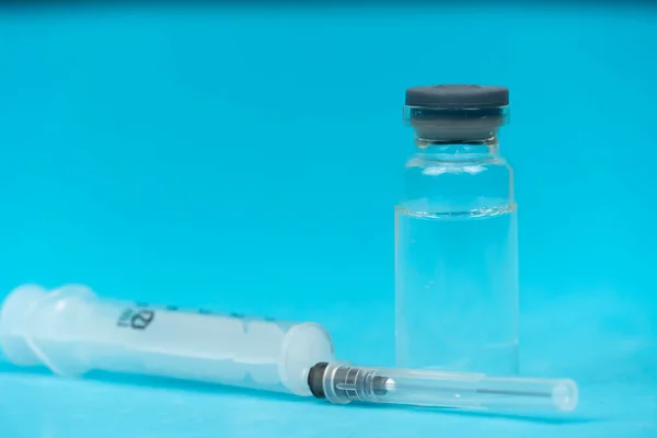 Medical glass bottle and plastic injection syringe on blue background close-up, copy space. Concept of medicine, vaccination, diabetes and cosmetic injections