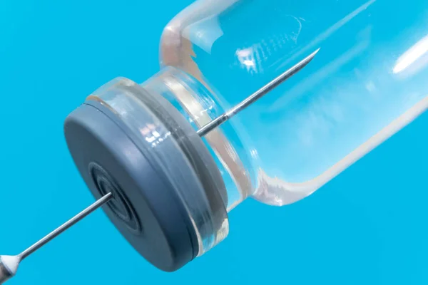 Syringe with a needle in a bottle of medicine on a blue background, macrophotography. Concept of medicine, vaccination