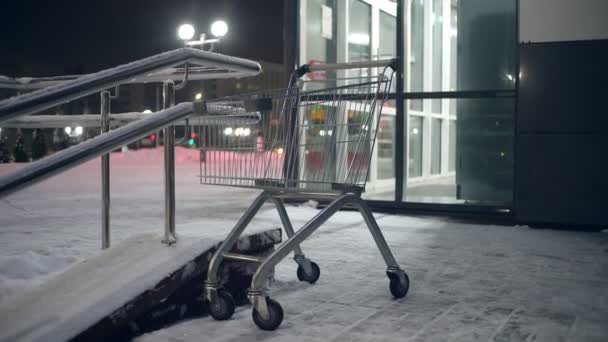 V noci stojí na parkovišti supermarketu v silném sněžení vozík s potravinami.