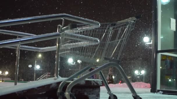 Een boodschappenkarretje staat 's nachts in een zware sneeuwval op de parkeerplaats van de supermarkt. — Stockvideo
