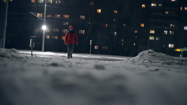 Kamera filmt vom Boden aus, Mann läuft im Winter durch nächtliche Stadt. — Stockvideo
