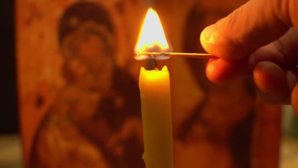 Bir adamın el feneri kilise mumunu bir ikonun arka planında kibritle yakar — Stok video