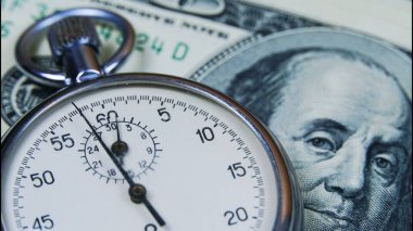 Kronometre 100 dolarlık banknotların üstünde ve el tik tak ediyor. Satışlar, indirimler ve hisse senedi ve iş yatırımları kavramı.