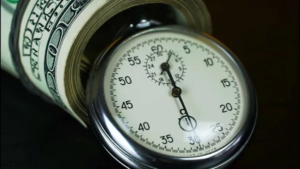 The stopwatch is on the table, next to it is a wad of 100 dollars bills rolled up with a rubber band, and the hand is ticking. The concept of sales, discounts and investments in stocks and businesses.