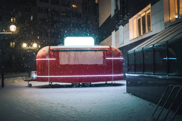 Beautiful red street food van with an illuminated white sign stands outside the building on a beautiful snowy winter evening. Fabulous beautiful winter evening, van