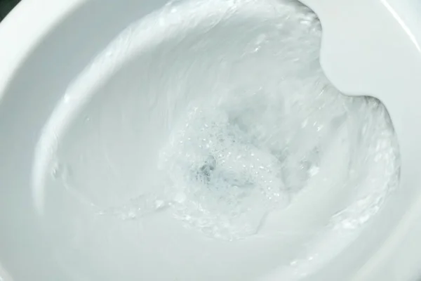 Close-up of flushing water in a white rimless toilet bowl