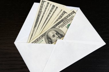 Siyah bir masanın üzerinde beyaz bir zarfın içinde Amerikan doları. Gelir, ikramiye ya da rüşvet kavramı. Yolsuzluk, maaş, ikramiyeler.