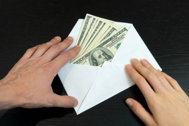 Erkek ve kadın eli, siyah arka planda dolar içeren bir zarf alır. Rüşvet, yardım ve ücret kavramı