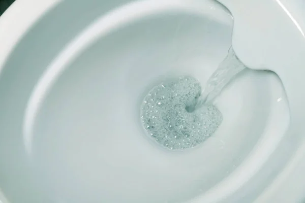 Close-up of flushing water in a white rimless toilet bowl