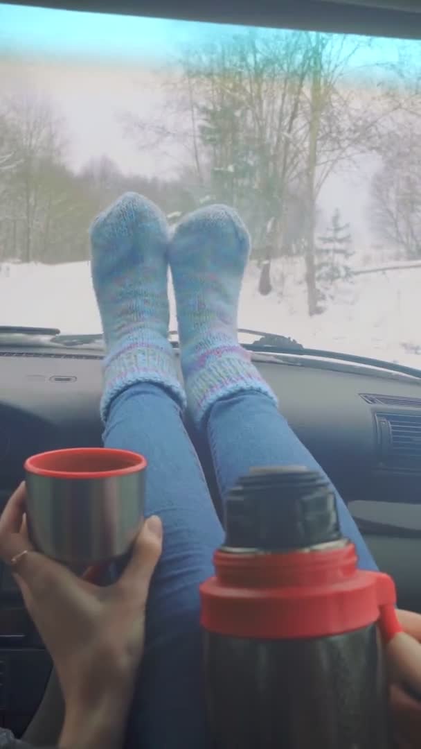 मुलगी थर्मोसमधून चहा पिते, डॅशबोर्डवर तिच्या पायांसह कारमध्ये बसून . — स्टॉक व्हिडिओ