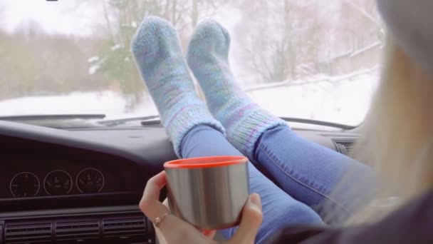 Fille boit du thé de thermos, assis dans la voiture avec ses pieds sur le tableau de bord. — Video