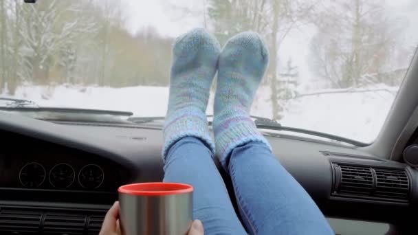 Dziewczyna pije herbatę z termosu, siedzi w samochodzie ze stopami na desce rozdzielczej. — Wideo stockowe