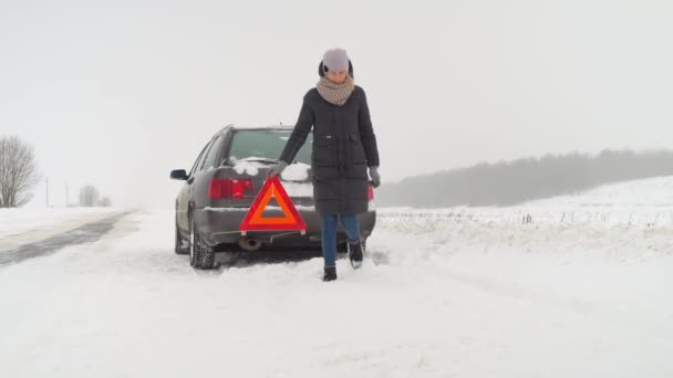 Kız kışın bozuk arabasının yanına acil durum levhası asıyor. — Stok video