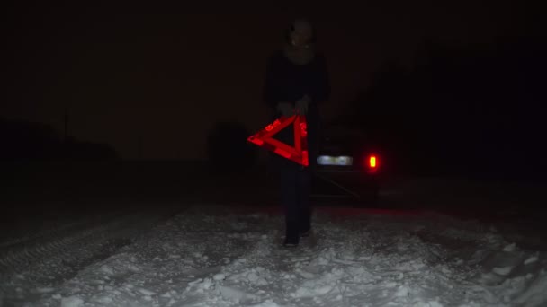 Een meisje zet een noodstopbord naast haar auto op een winteravond. — Stockvideo