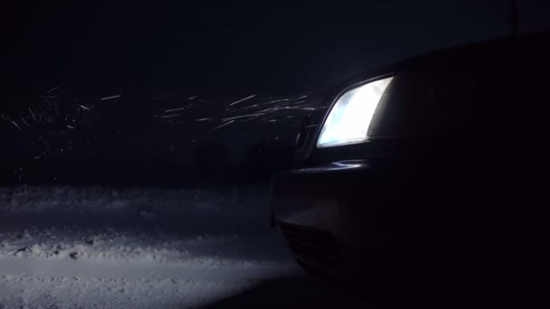 Le phare de la voiture brille la nuit. Des flocons de neige y volent, un vent fort — Video