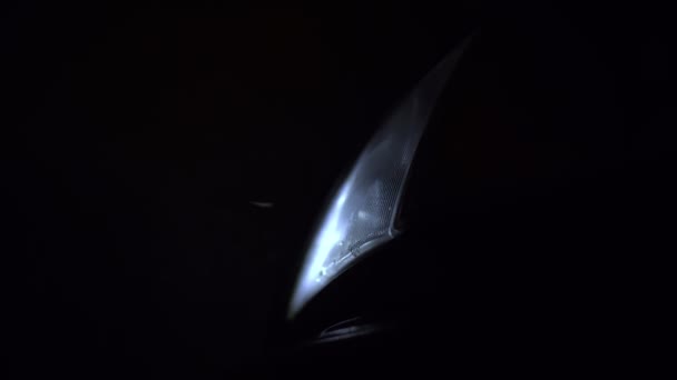 The car's headlight shines at night. Snowflakes fly into it, a strong wind — Stock Video