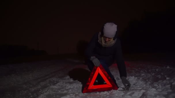 Una chica pone una señal de parada de emergencia junto a su coche en una noche de invierno. — Vídeos de Stock