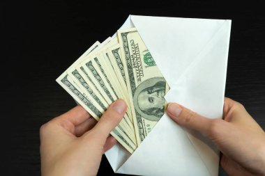 Kadınların elleri siyah arka planda beyaz bir zarftan dolar çeker. Rüşvet, maaş, zula kavramı