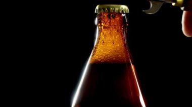 Erkek eli bir şişe bira açar. Kapağın altından bira köpüğü fışkırıyor..