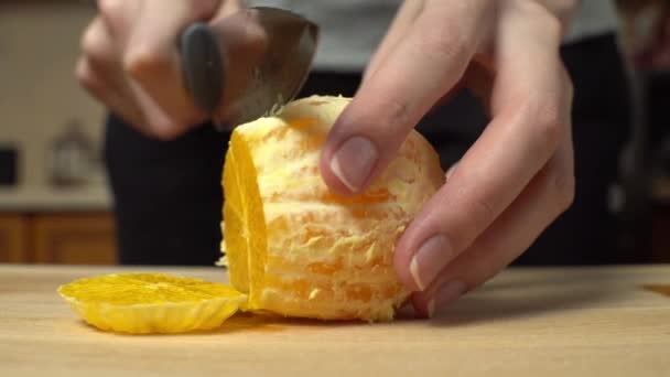 Primer plano de las manos de una mujer en una cocina casera cortando una naranja pelada. — Vídeos de Stock