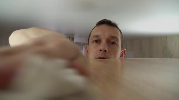 Koncepce úklidu domu. muž utírá prach z vysoké skříňky ve svém domě — Stock video