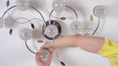 Genç bir adam, bir elektrikçi, avizedeki lambayı değiştiriyor..