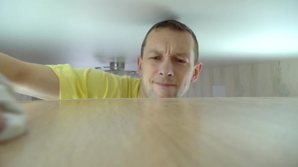 Концепція прибирання будинку. чоловік витирає пил з високої шафи в своєму будинку — стокове відео