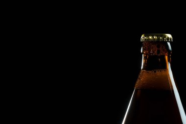 Siyah zemin üzerinde metal kapağı olan kahverengi bira şişesine yakın plan.
