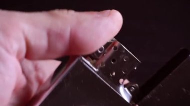 Bir adamın eli bir benzin çakmağı açar ve bir zippo yakar.