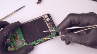 Bir teknisyen ya da usta cep telefonunu tamir eder, kabloyu söker, ana kartın kablosunu ve koruyucusunu koparır. Eller, eldivenler. Bir makro. Yakın plan..