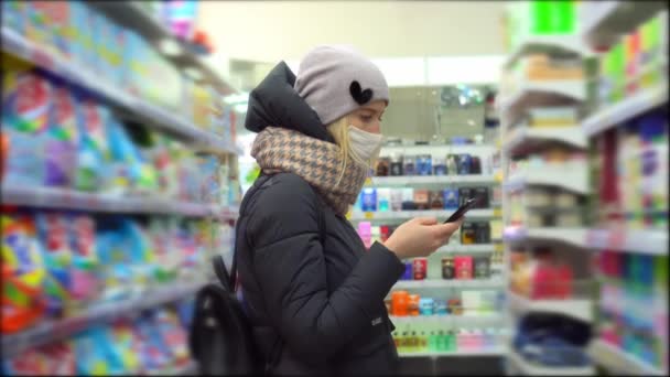 Μια μασκοφόρος γυναίκα κάνει αγορές και ελέγχει τη λίστα αγορών της από το smartphone της — Αρχείο Βίντεο