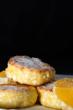 Beyaz bir tabakta portakal dilimli tatlı peynirli kekler fotokopi alanı olan siyah bir duvara yakın plan. Dikey fotoğraf