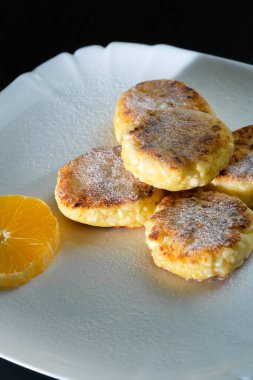 Pudra şekerli leziz süzme peynir krepleri. Beyaz tabakta portakal da var. Dikey fotoğraf