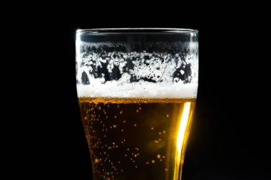 Siyah arka planda köpüklü bir bira bardağının yakın çekimi.