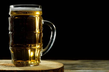 Açık bira bardağının yakın plan resmi. Siyah arka planda, ahşap bir stantta fotokopi alanı olan.