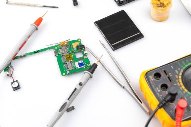 Radyo mühendisliği ustası cep telefonunun bir kısmını onarıp dijital multimetre ile ölçüm yapıyor.