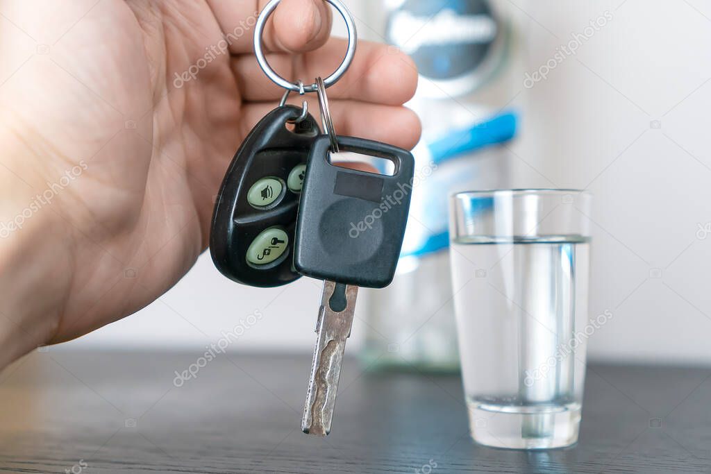 Man's hand takes the car keys and defiantly shows them to the camera against the background of a stack of vodka. Concept of drunk driving