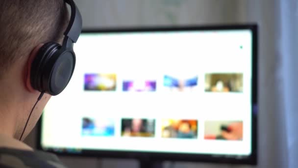 Facet ze słuchawkami patrzy na monitor komputera i surfowanie w Internecie. — Wideo stockowe