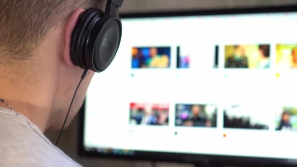 Mann mit Kopfhörer schaut auf Computermonitor und surft im Internet. — Stockvideo