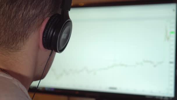 ヘッドフォンの男はモニターを見て慎重に画面上のグラフに従います. — ストック動画