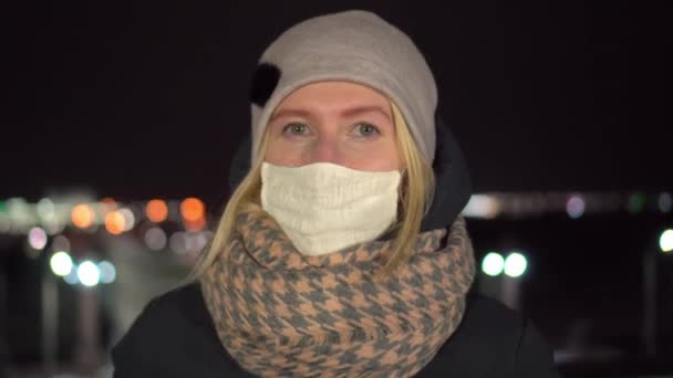 Flicka i mask tittar på kameran på natten mot bakgrund av natten stad. — Stockvideo