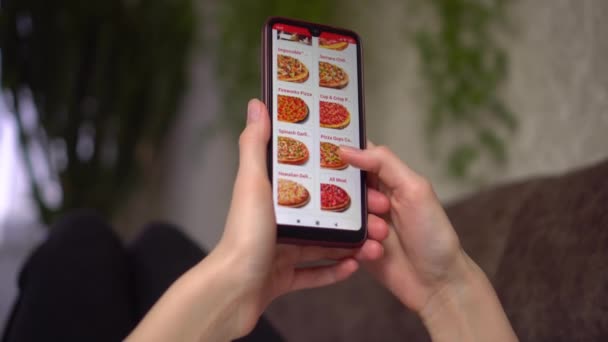 Una mujer pide comida en casa desde una tienda en línea, un teléfono inteligente — Vídeos de Stock